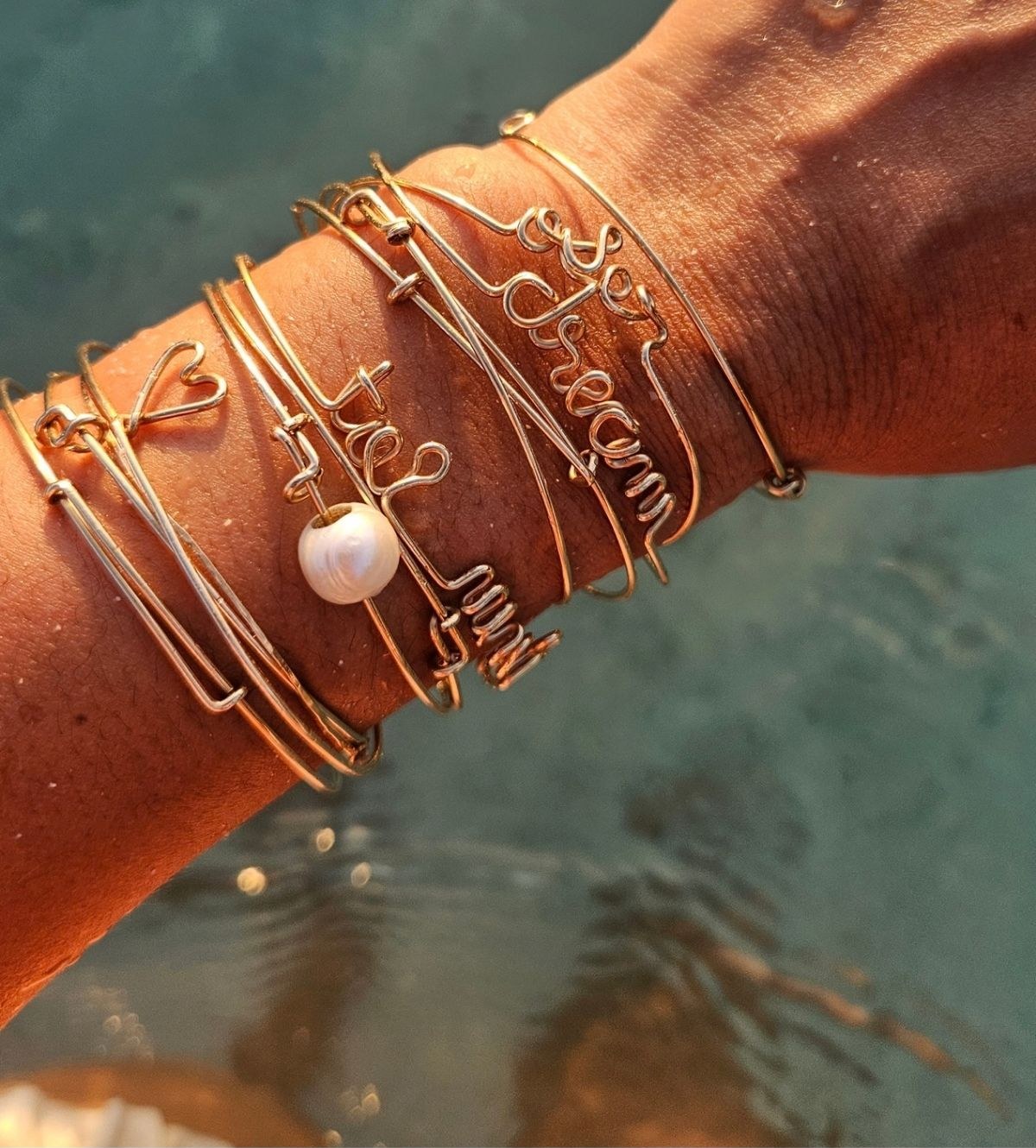 A stack of Lou Dot Lou Bijoux gold wire bangles with a pearl, worn on a wrist