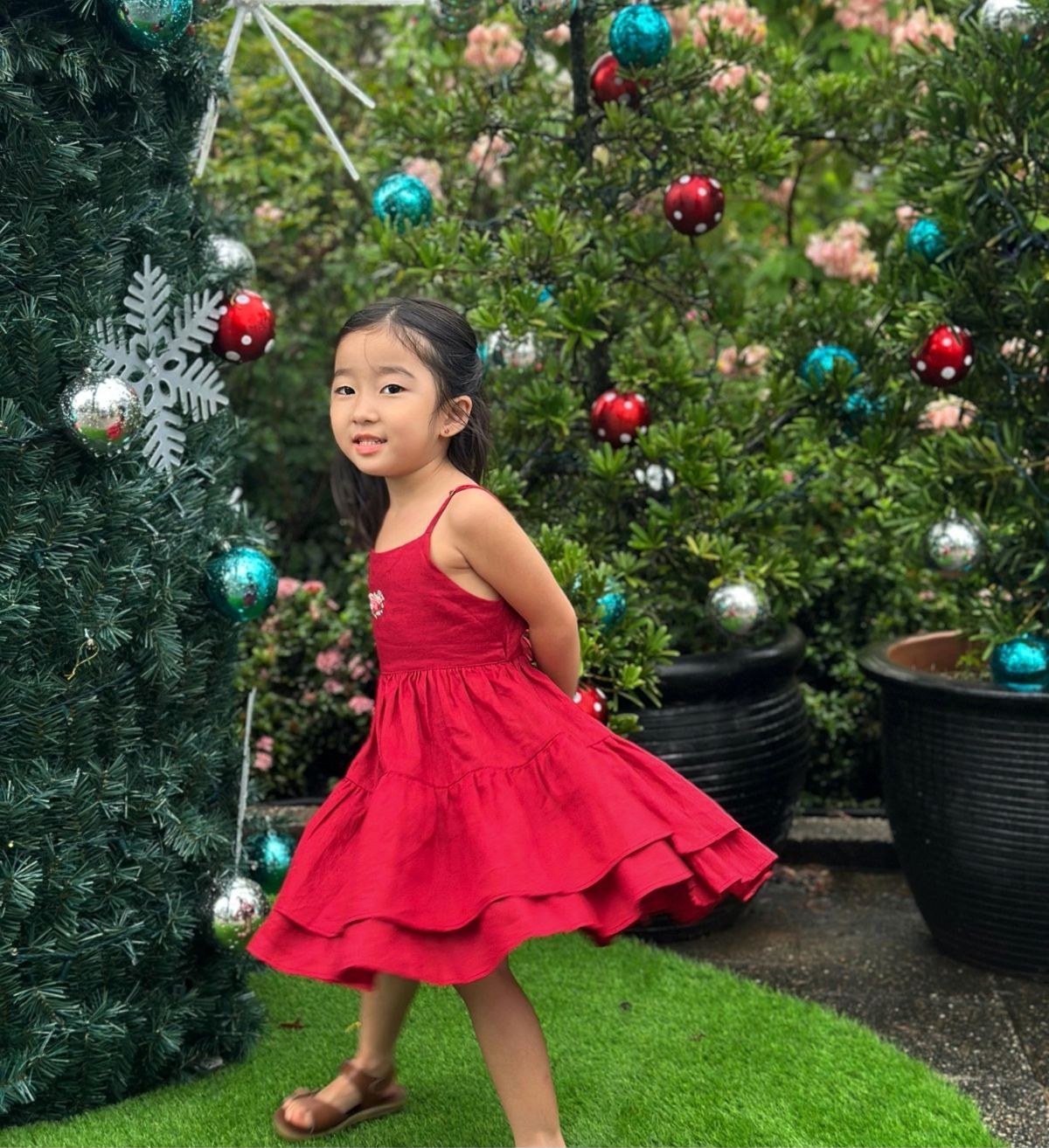A girl twirling in a red tiered dress in front of a decorated Christmas tree