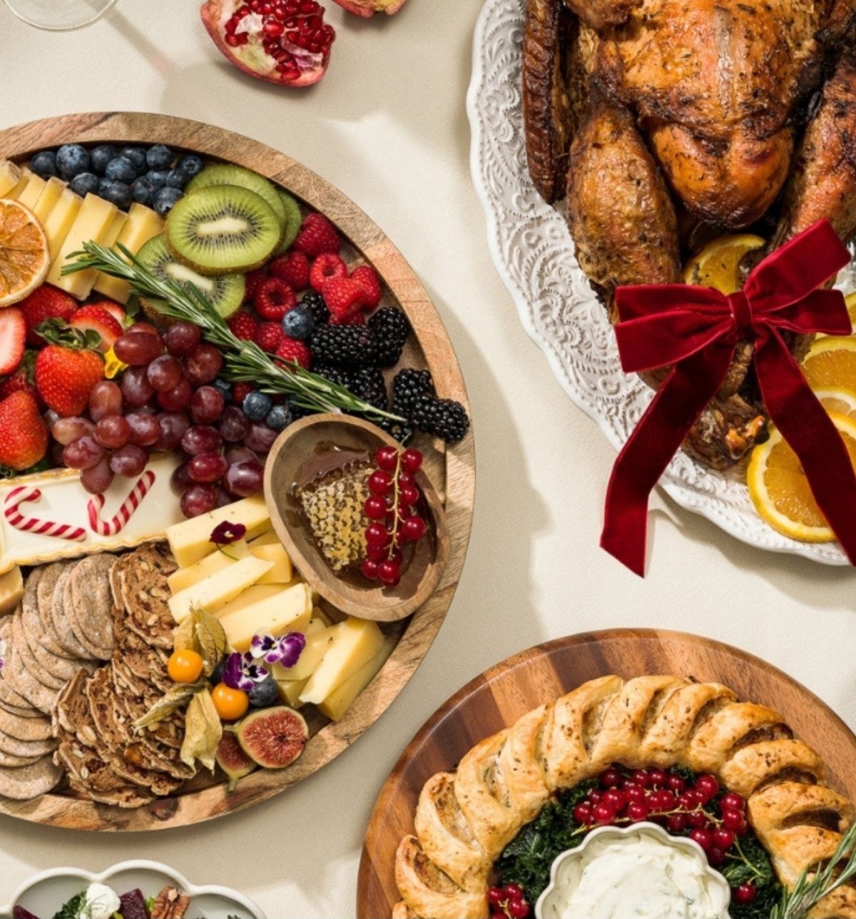 A festive grazing platter of fruit, cheese and crackers beside a roast with a red velvet bow