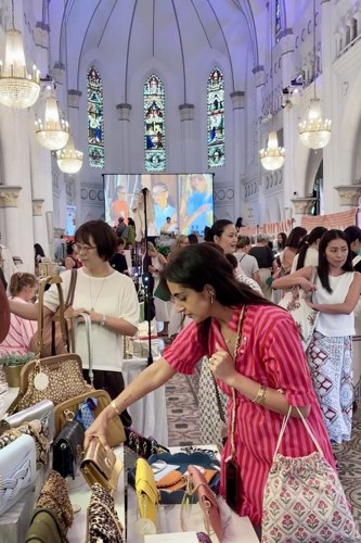 A shopper browsing a table of bags and accessories at a busy stall